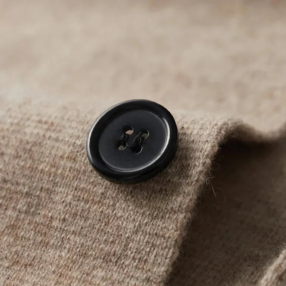 Close-up of black horn-style button on beige cashmere blazer cardigan