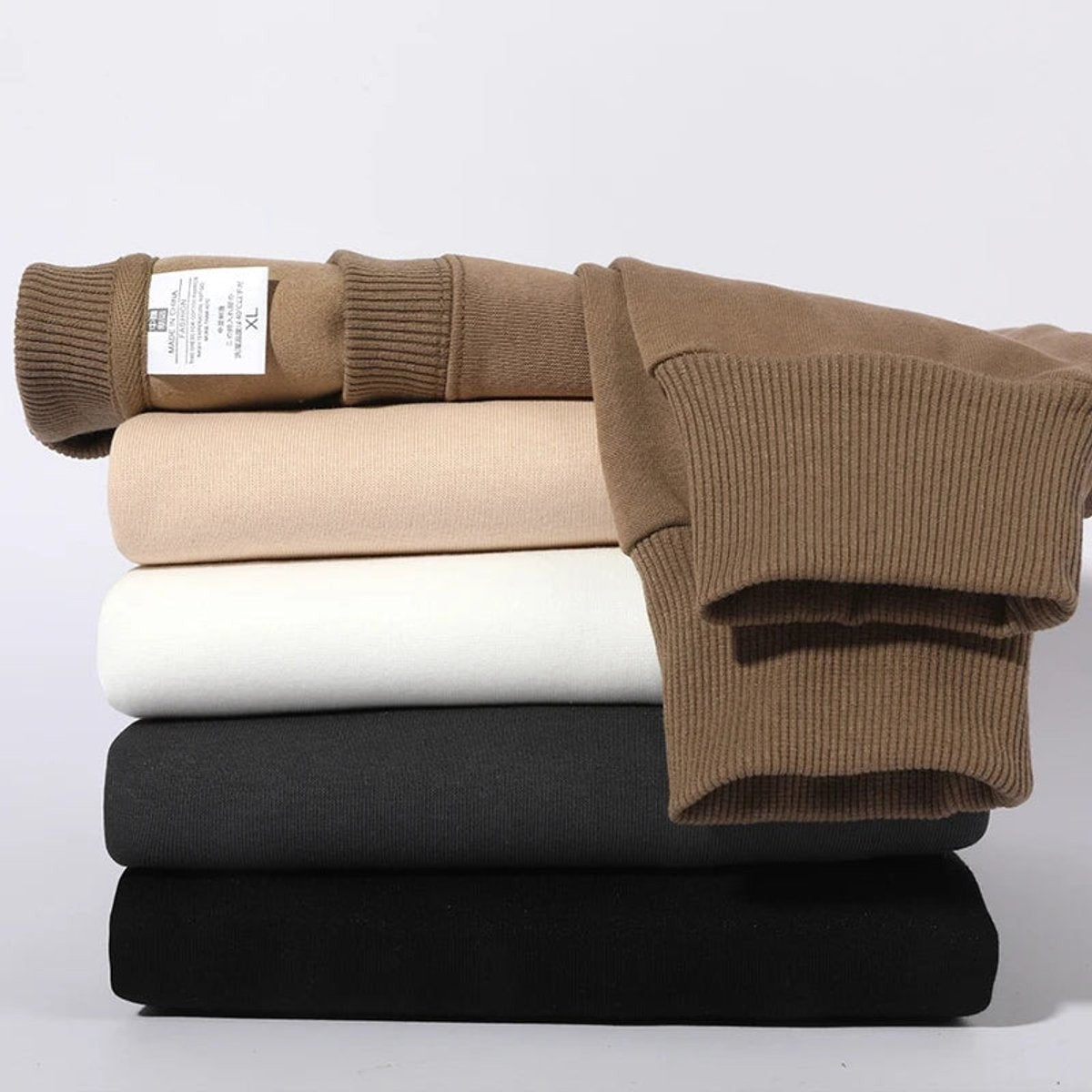 Folded stack of crewneck jumpers in camel, beige, white and black shades