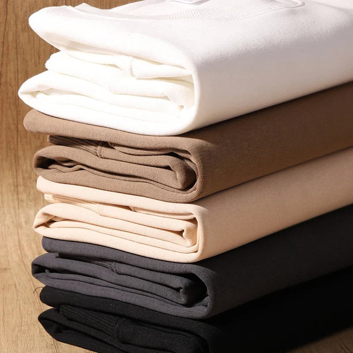 Neatly folded cotton fleece jumpers showing white, camel, beige and black colourways