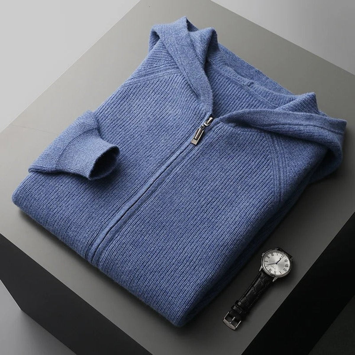 Folded blue knitted zip cardigan jumper displayed with a leather wristwatch