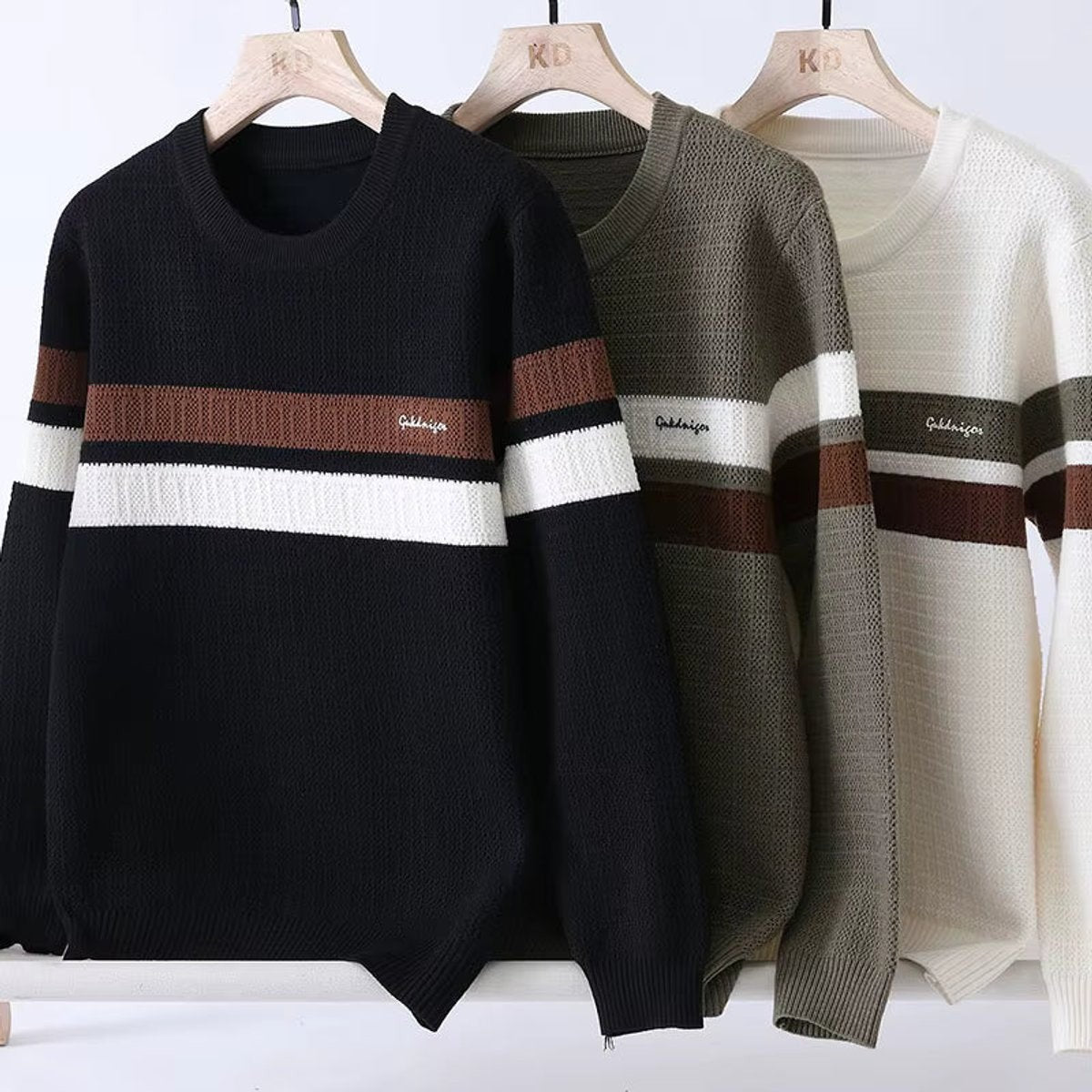Three heritage stripe jumpers in black, khaki and cream on hangers