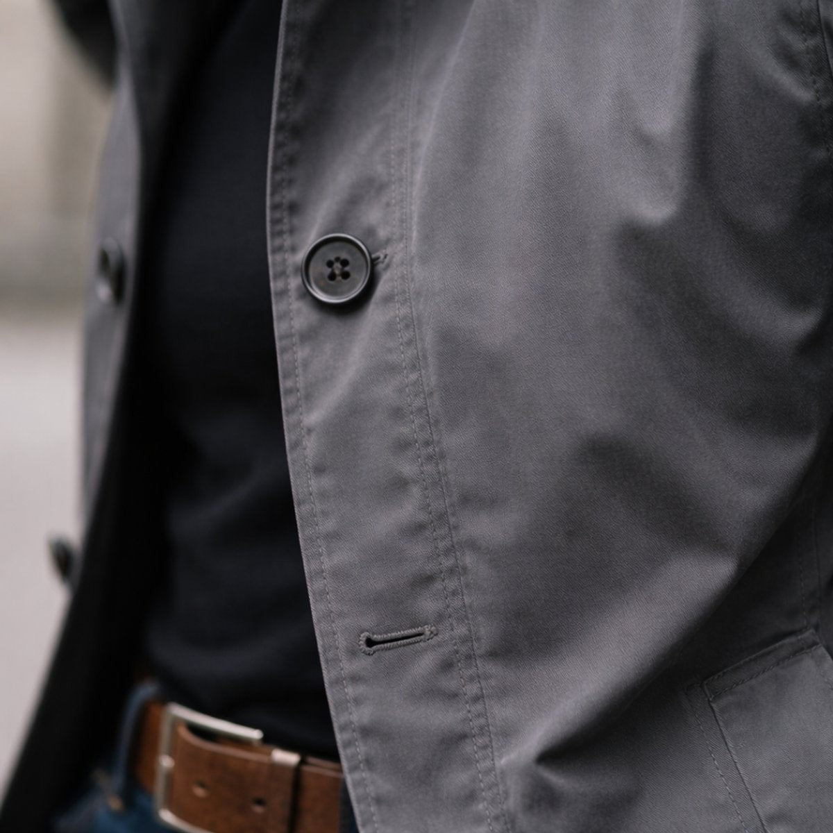 Close-up of grey overcoat fabric showing button and stitched buttonhole detail