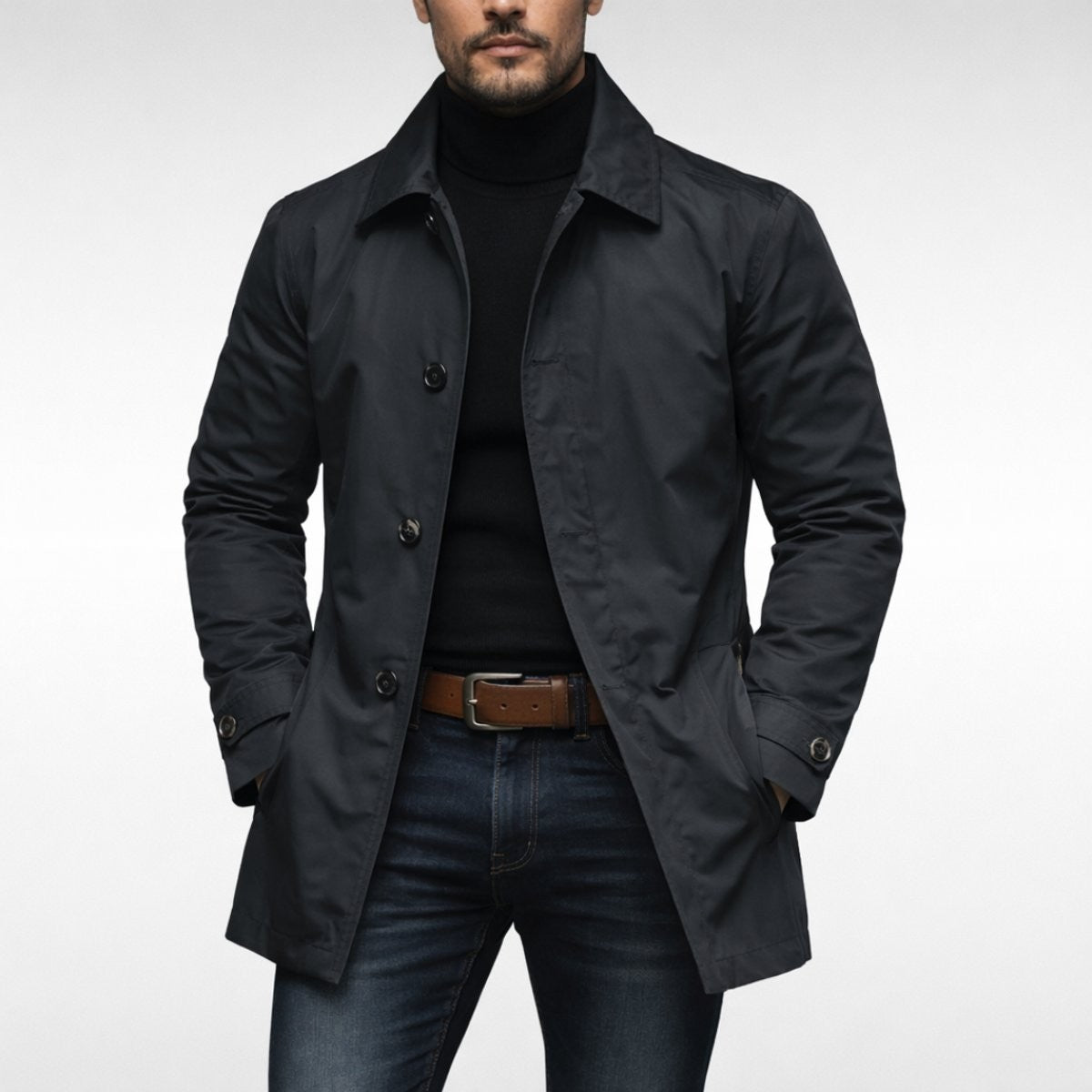 Charcoal weather-resistant overcoat worn open over black jumper and dark denim