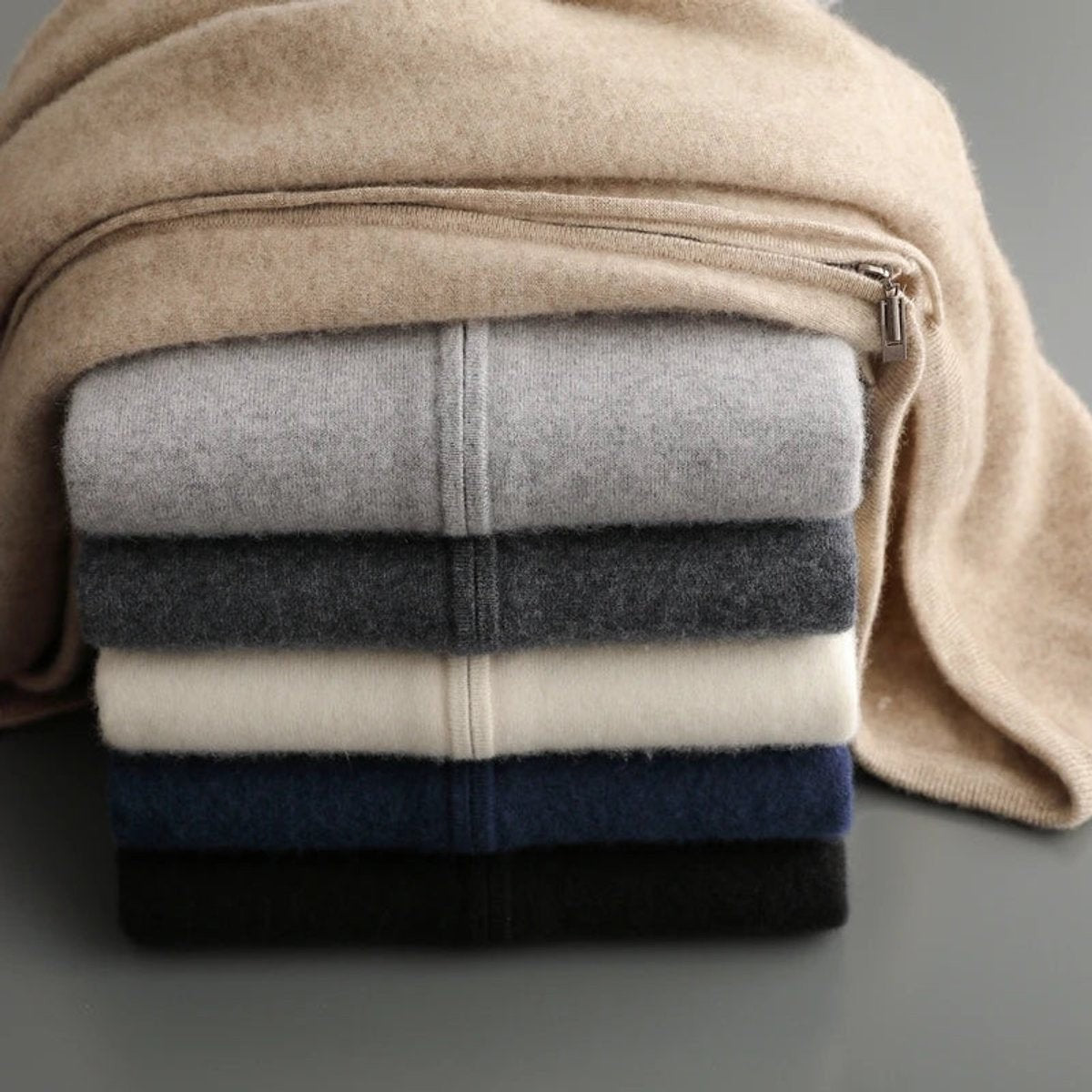 Beige knitted hoodie draped beside neatly stacked folded jumpers in various colours