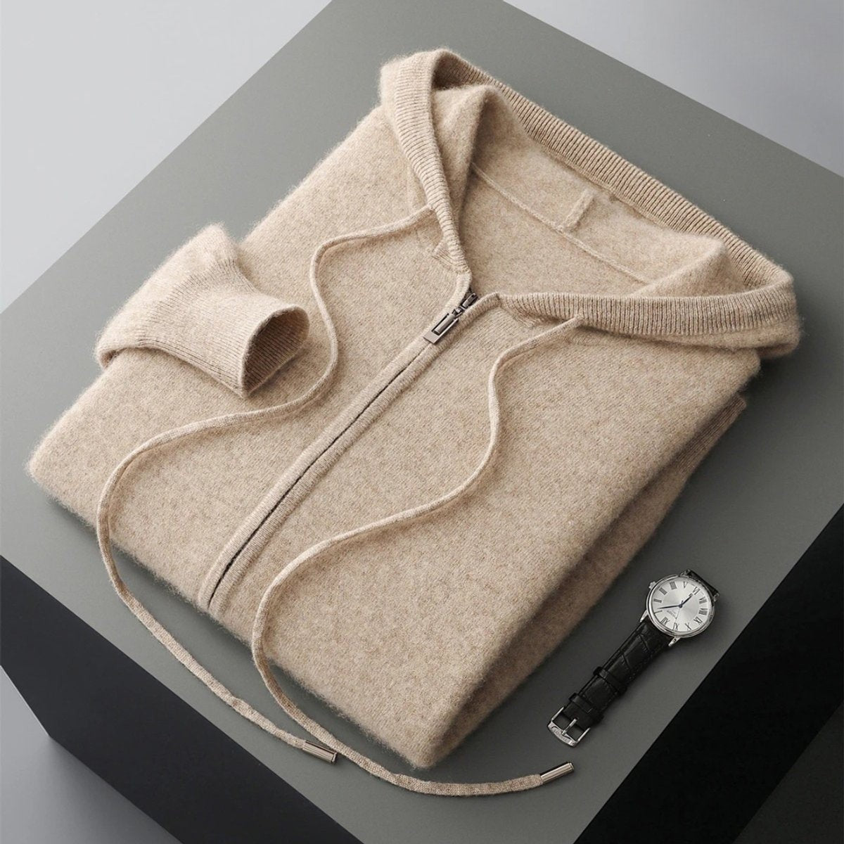 Folded beige cashmere knit zip hoodie with drawstring hood beside a wristwatch