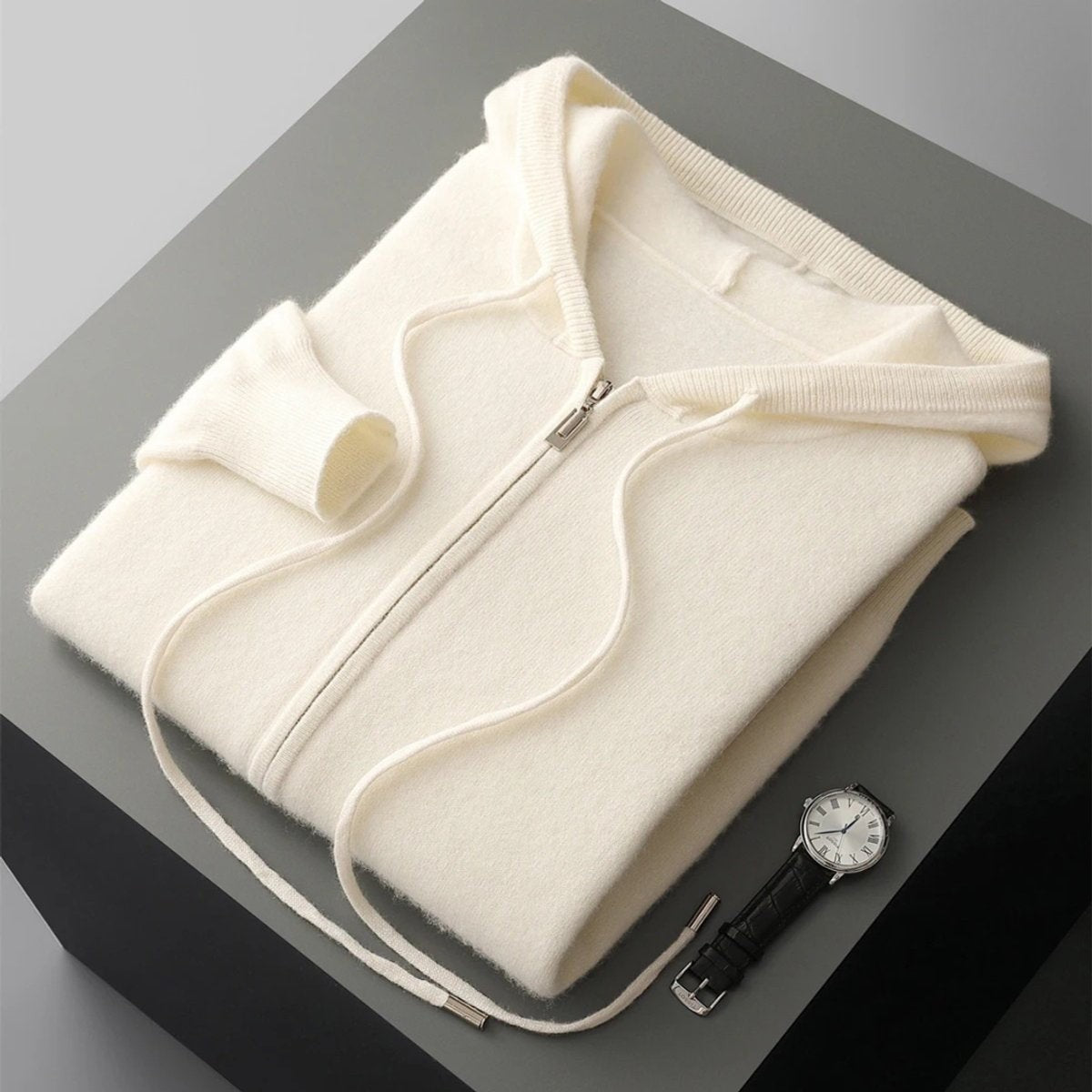 Folded cream cashmere knit zip hoodie with ribbed trim beside a wristwatch