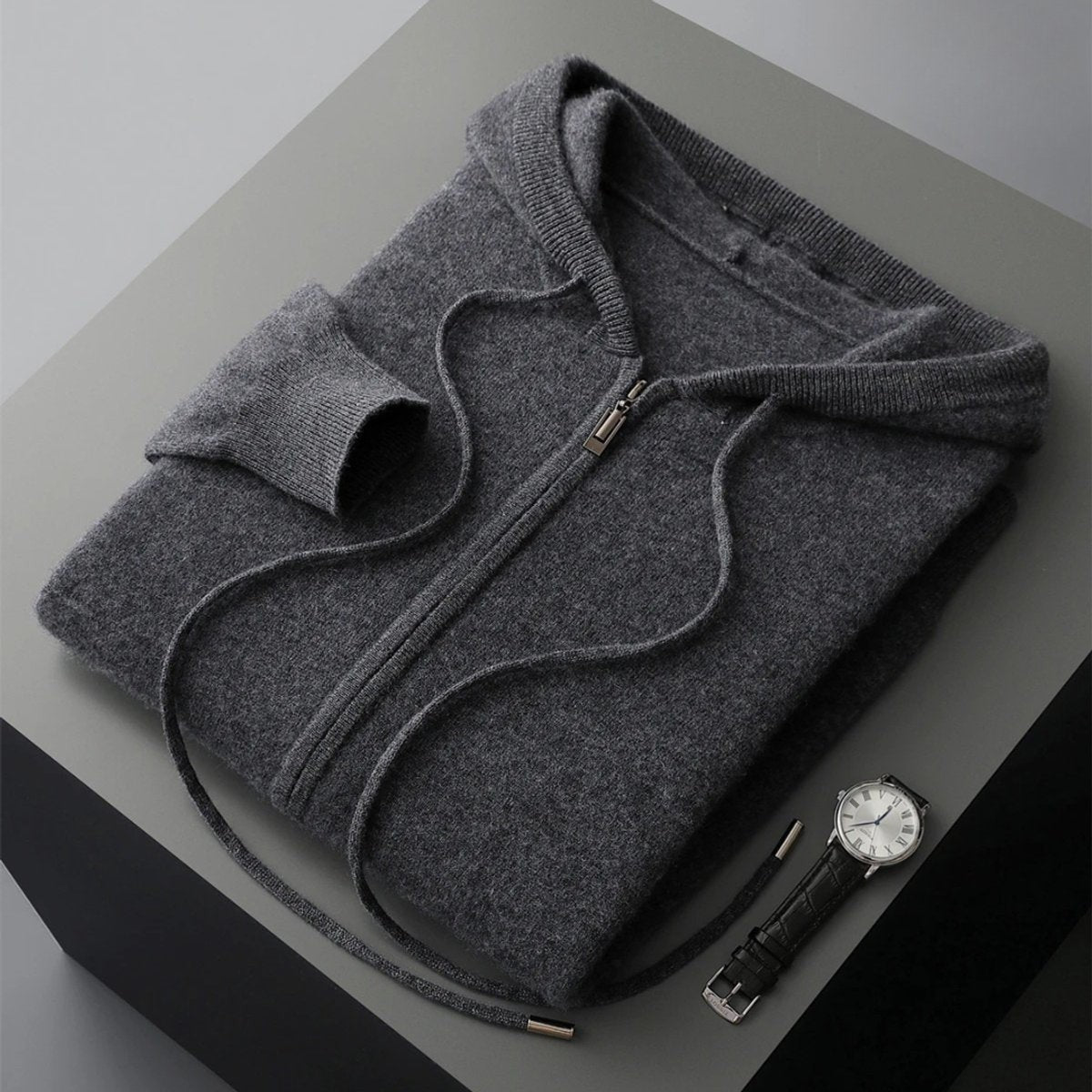 Folded charcoal grey cashmere knit zip hoodie with drawstring beside a wristwatch