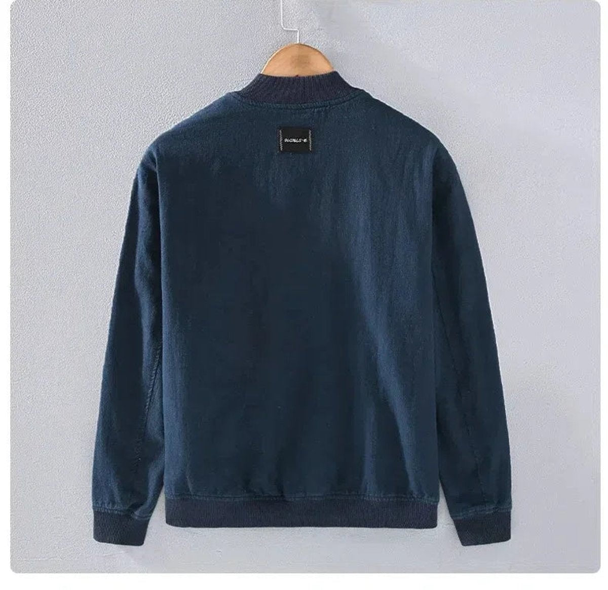 Rear view of navy ribbed-cuff bomber jacket on wooden hanger