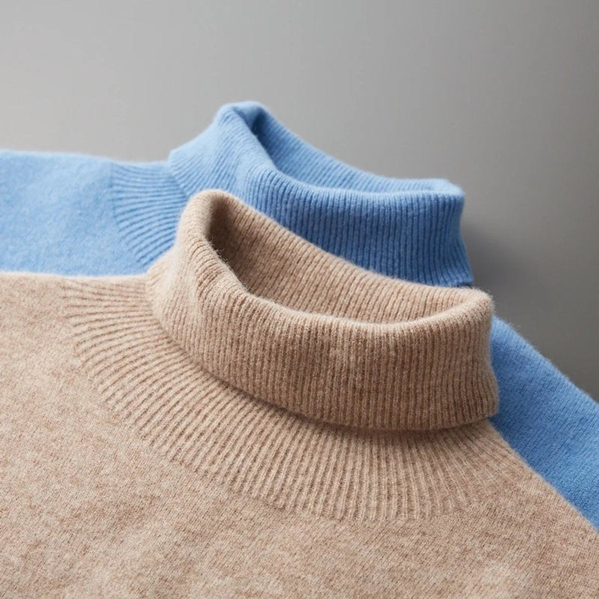 Folded blue and beige turtleneck jumpers showing ribbed collar detail