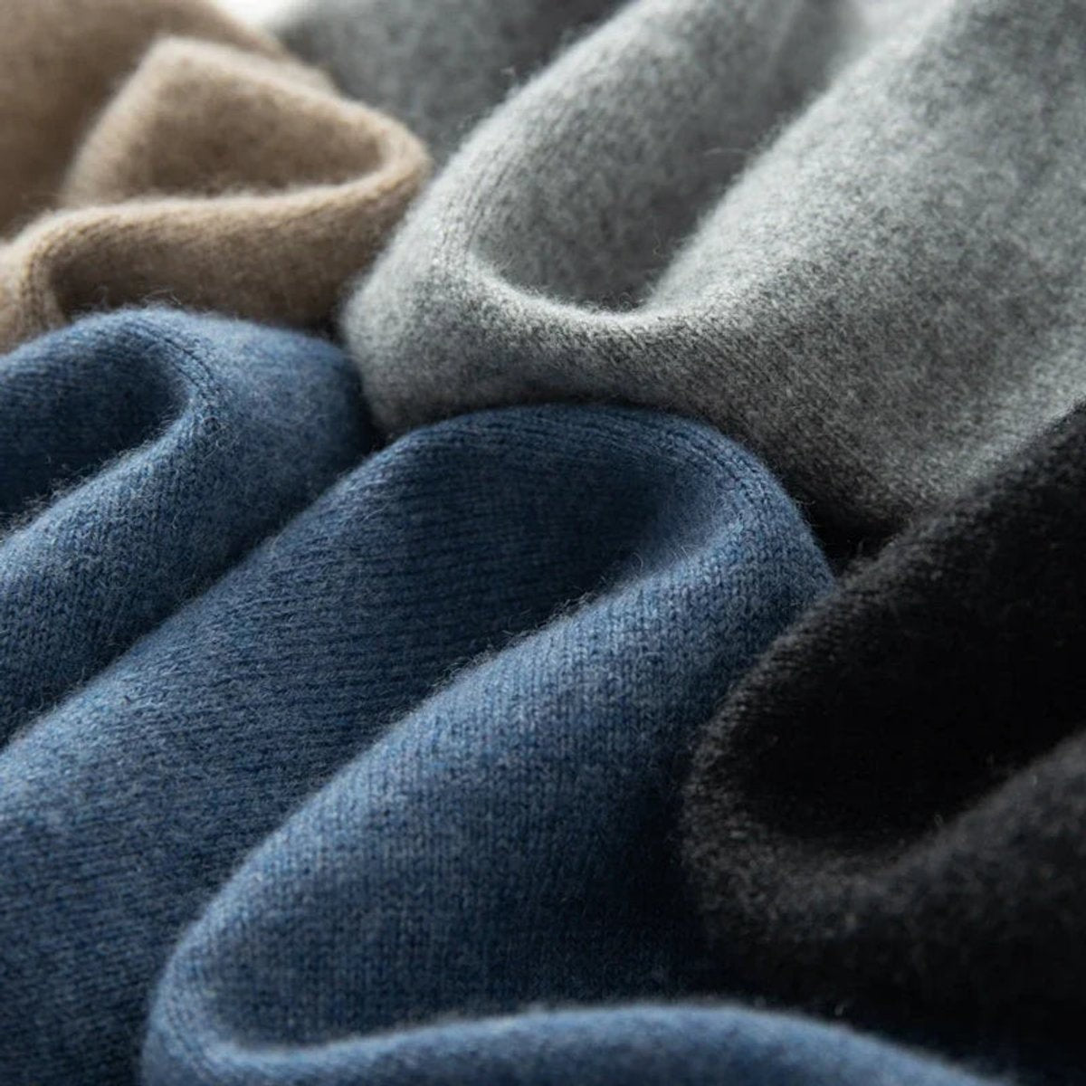 Stack of folded knitted jumpers in navy, grey, camel and black shades