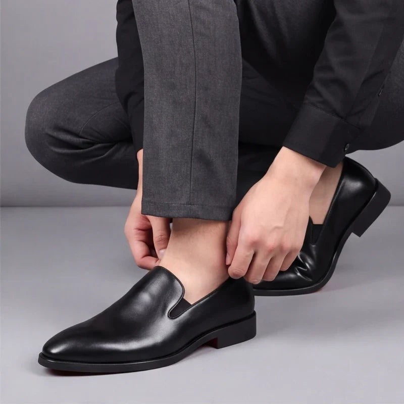 Man crouching to adjust black leather loafers with red sole