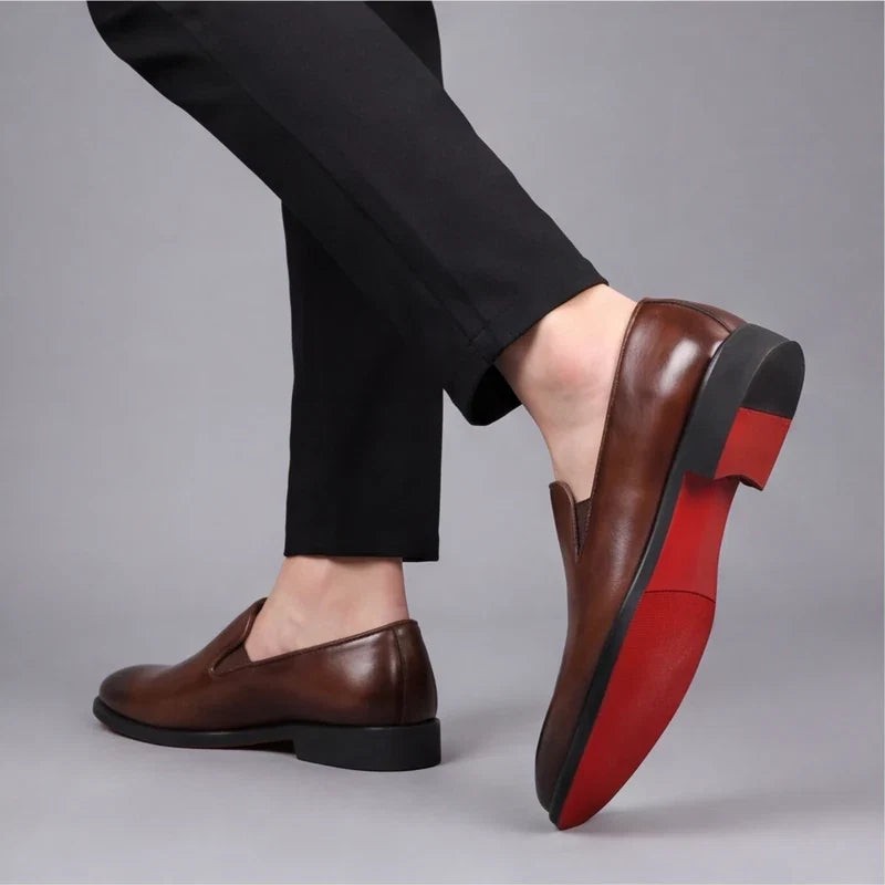 Model lifting foot to reveal red sole of brown leather loafer