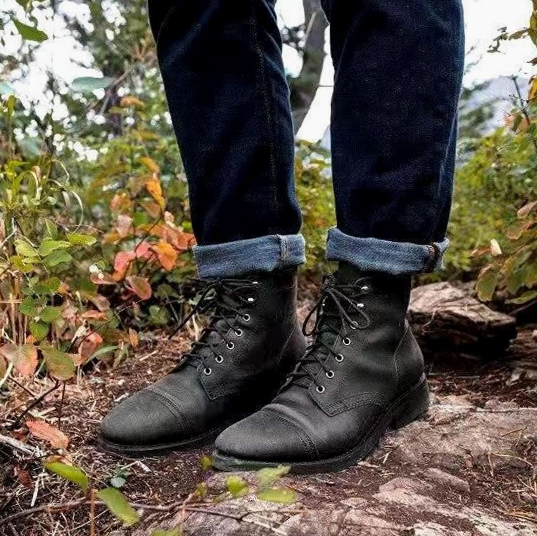 Men's black leather lace-up boots worn with turned-up dark denim jeans