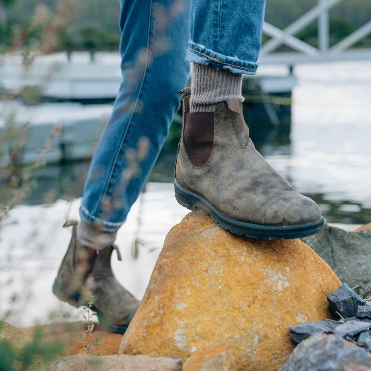 Model wearing rustic brown leather Chelsea boots while stepping on rocks outdoors