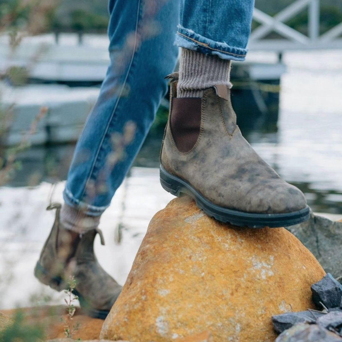 Model wearing distressed brown leather Chelsea boots on a rock outdoors