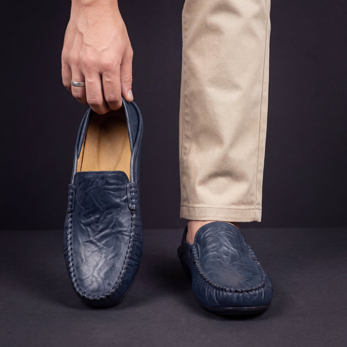 Man carrying navy leather moccasin alongside foot wearing matching slip-on