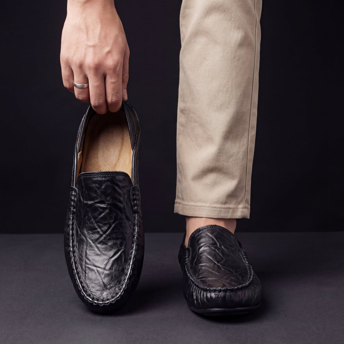 Man holding black leather moccasin beside foot wearing matching loafer