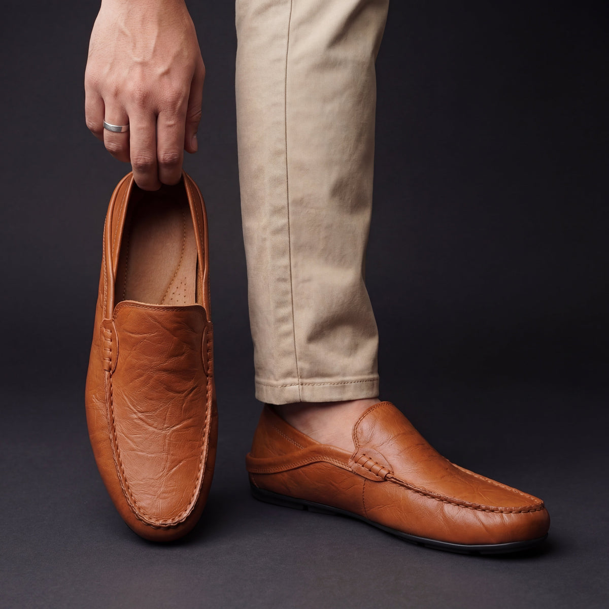 Tan leather loafer held by hand beside model wearing matching shoe