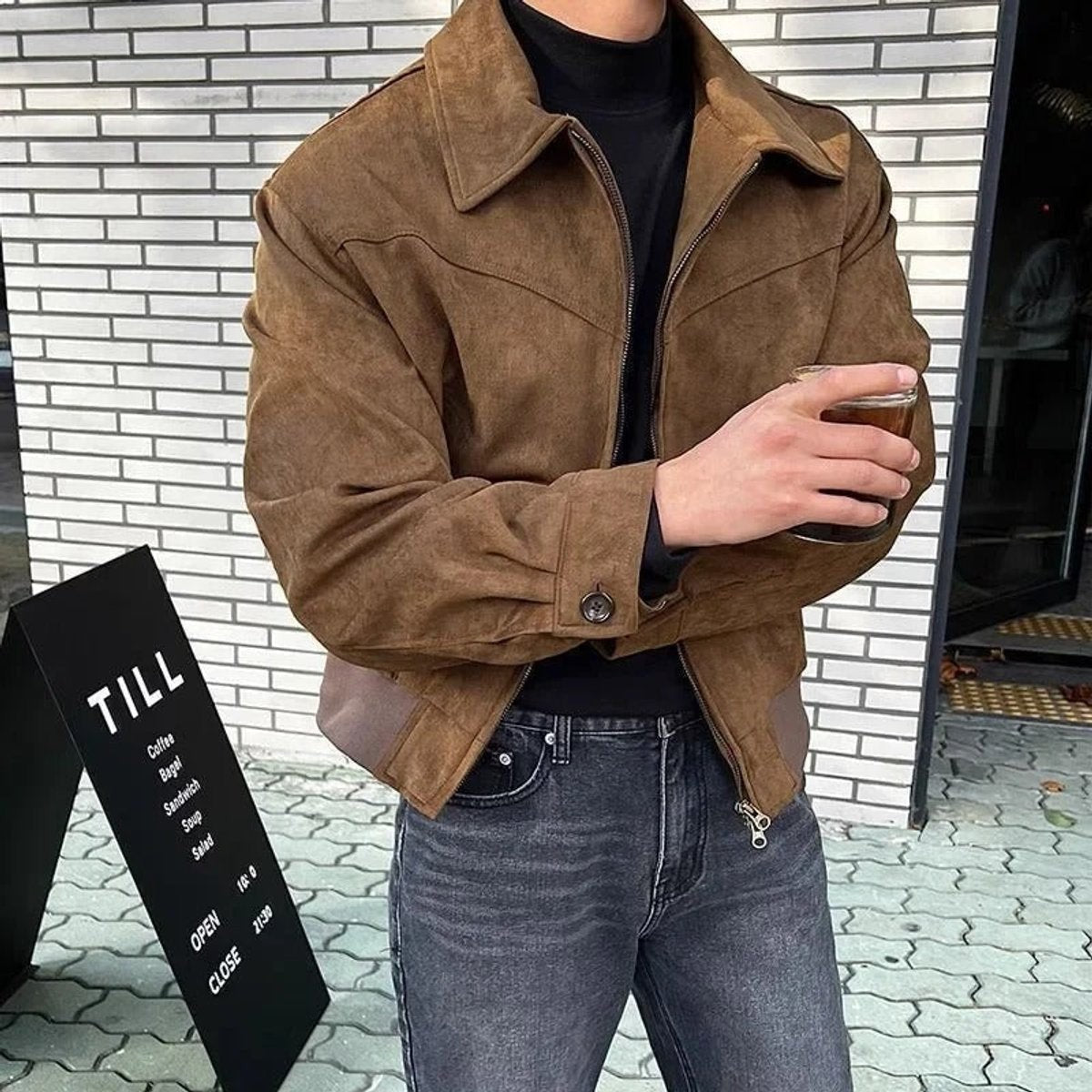 Model in tan suede bomber jacket holding drink outside coffee shop