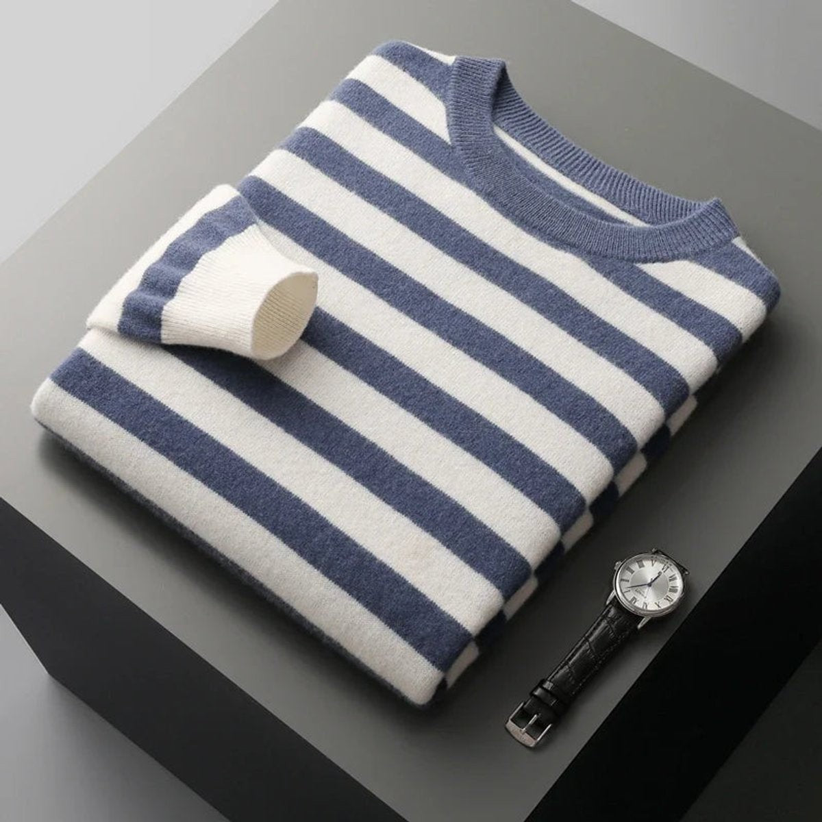 Folded navy striped knitted jumper beside classic leather watch