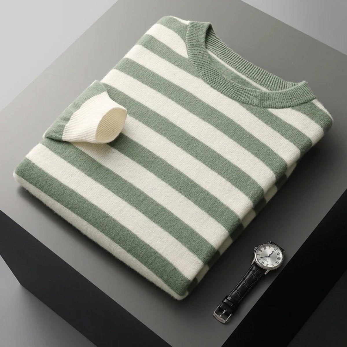 Sage green striped knitted jumper folded neatly with wristwatch