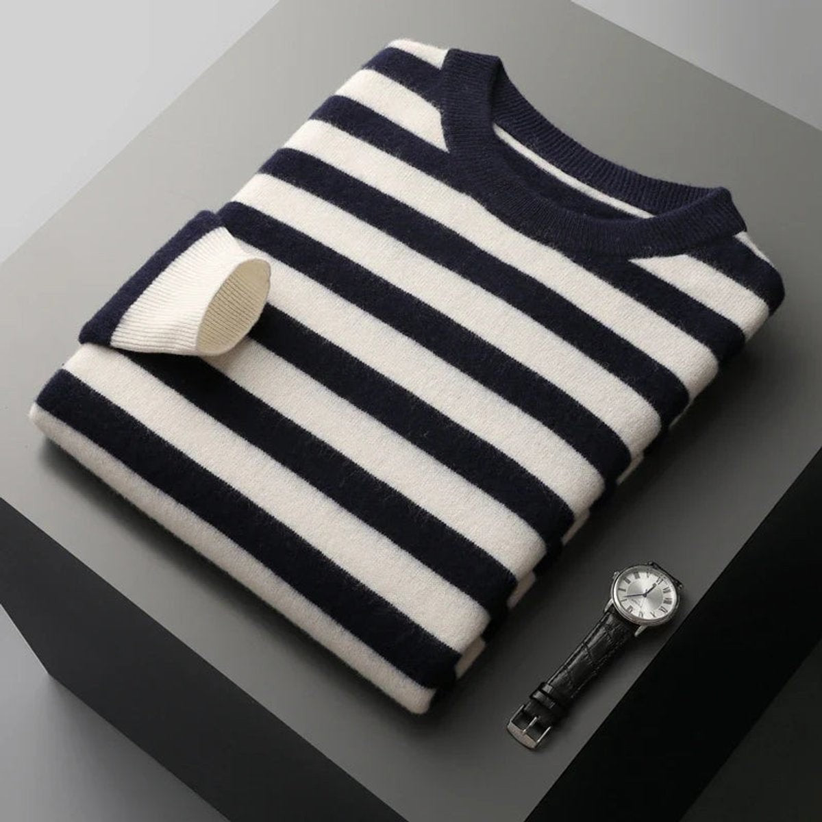 Dark navy striped knitted pullover folded beside leather-strap watch