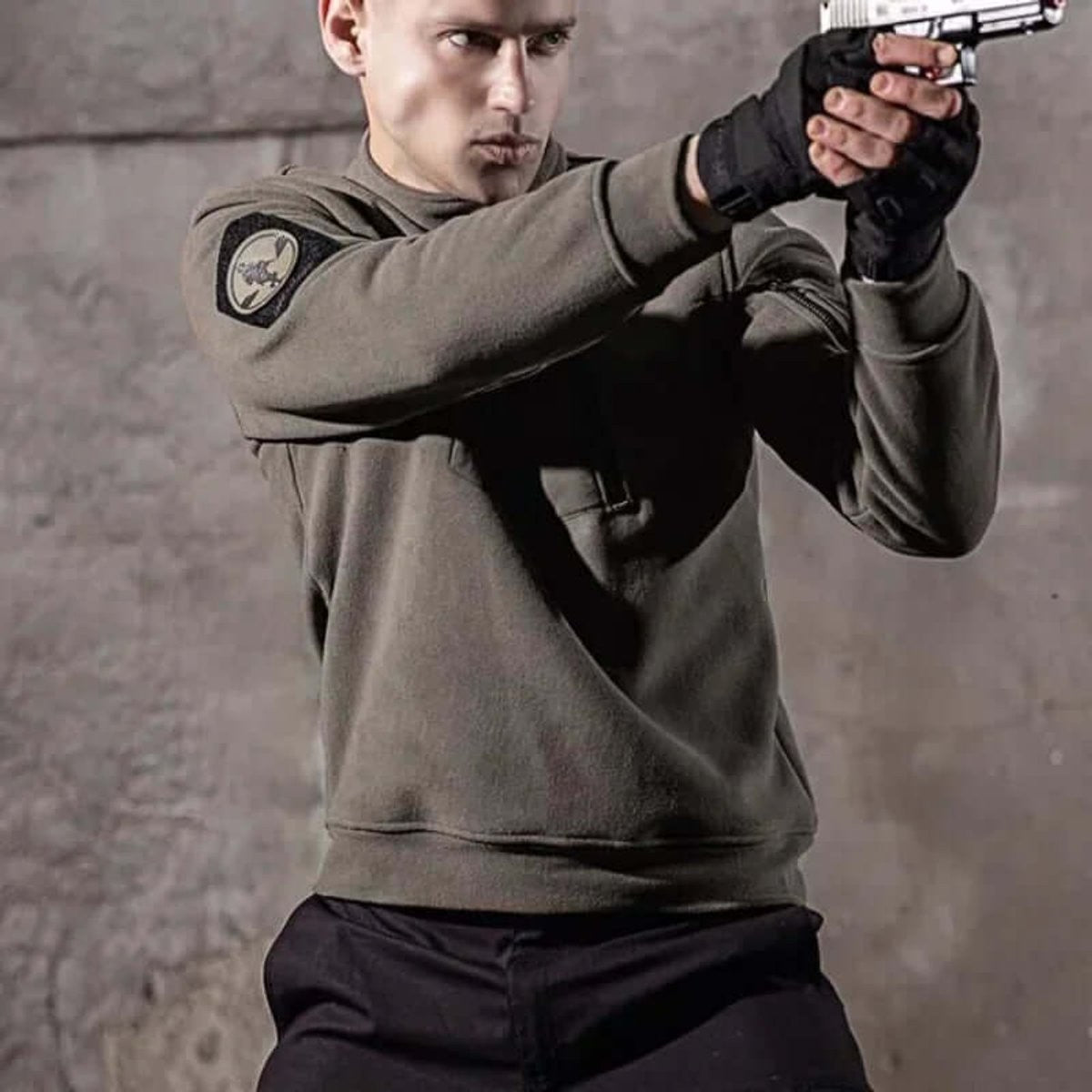 Man wearing olive tactical fleece jacket while aiming a pistol