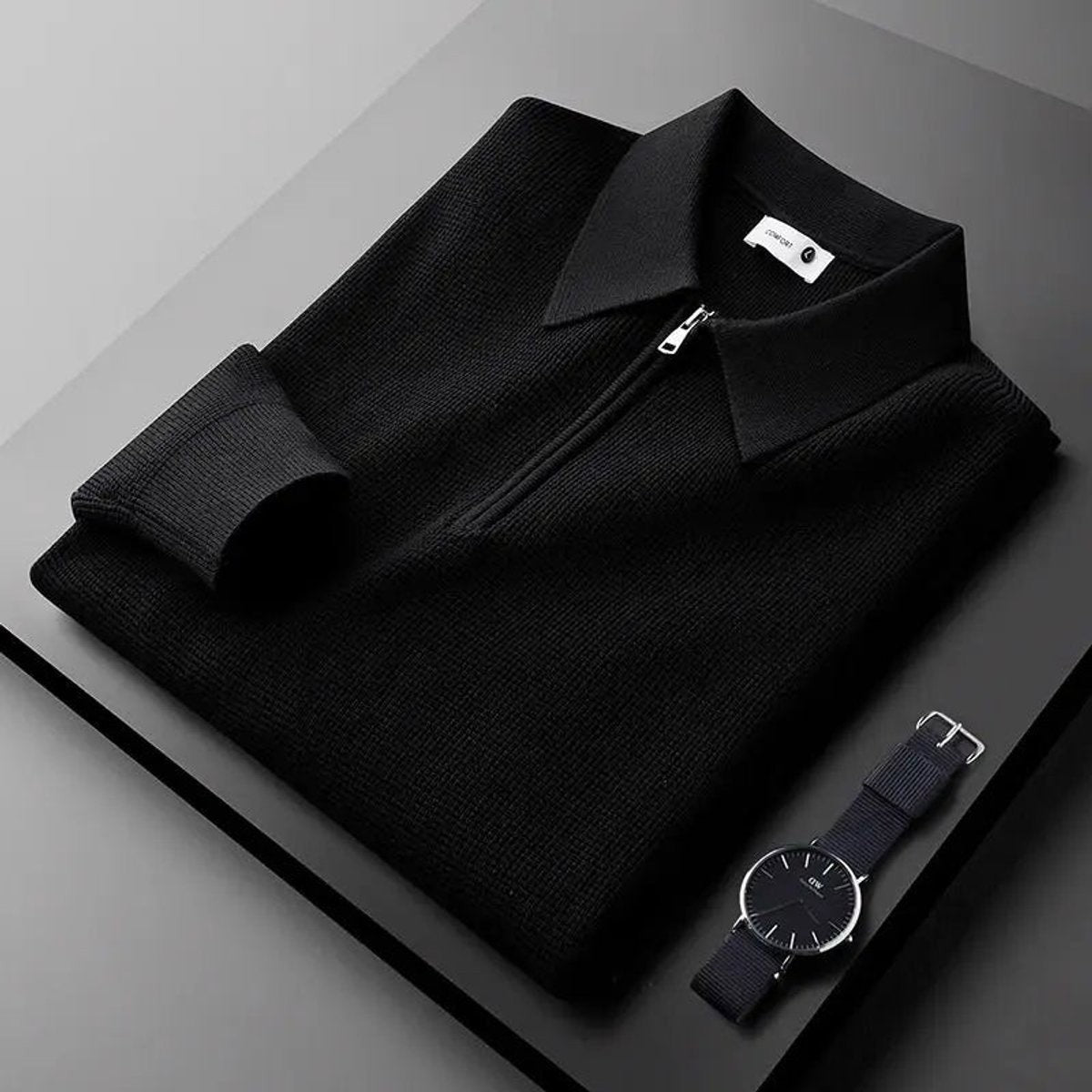 Black quarter-zip knitted polo jumper folded neatly with a wristwatch