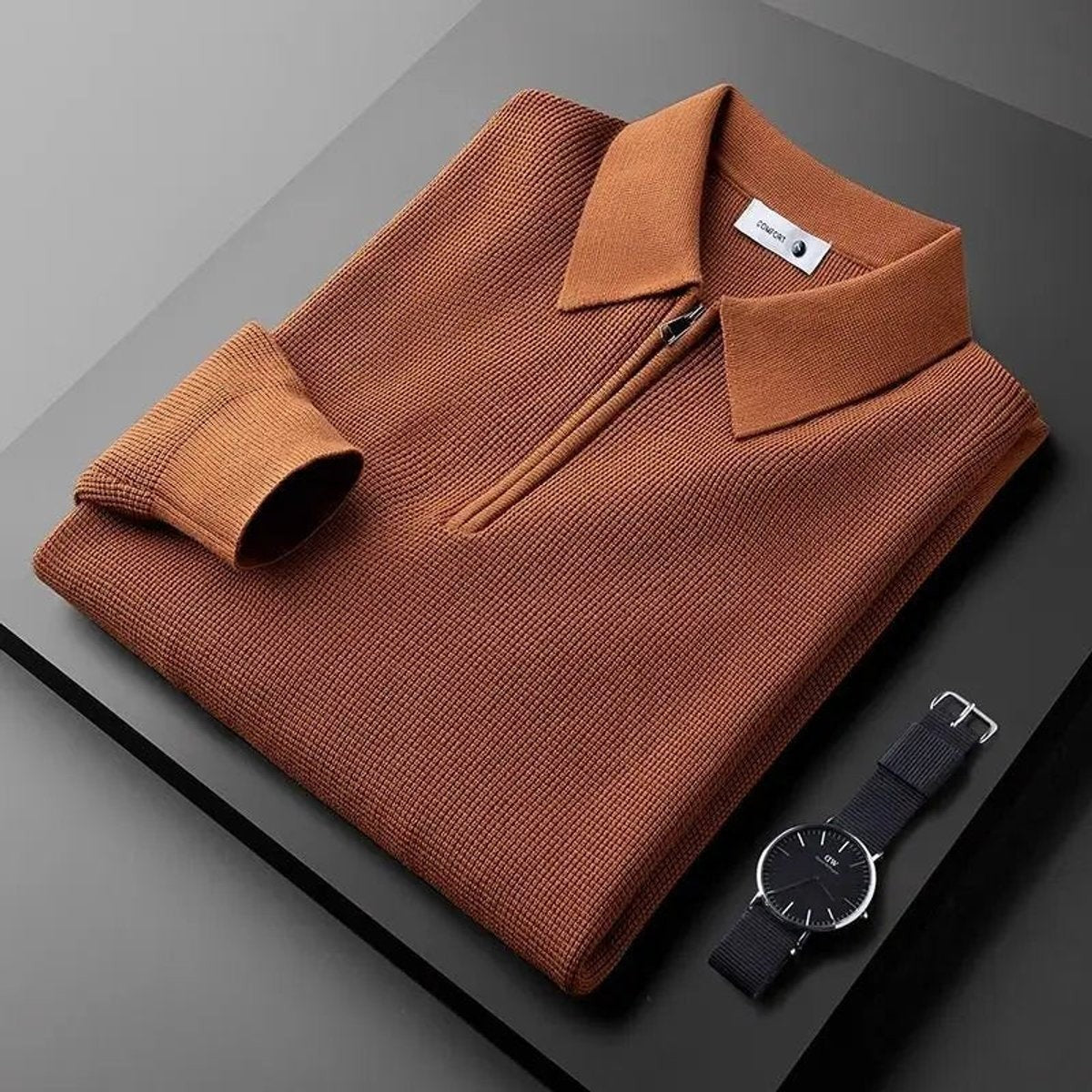 Rust-brown quarter-zip knitted polo jumper folded with a wristwatch
