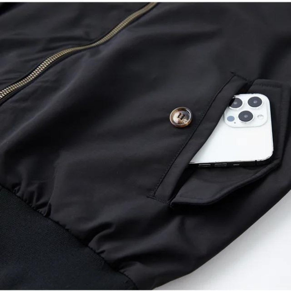 Close-up of black bomber jacket flap pocket holding a smartphone