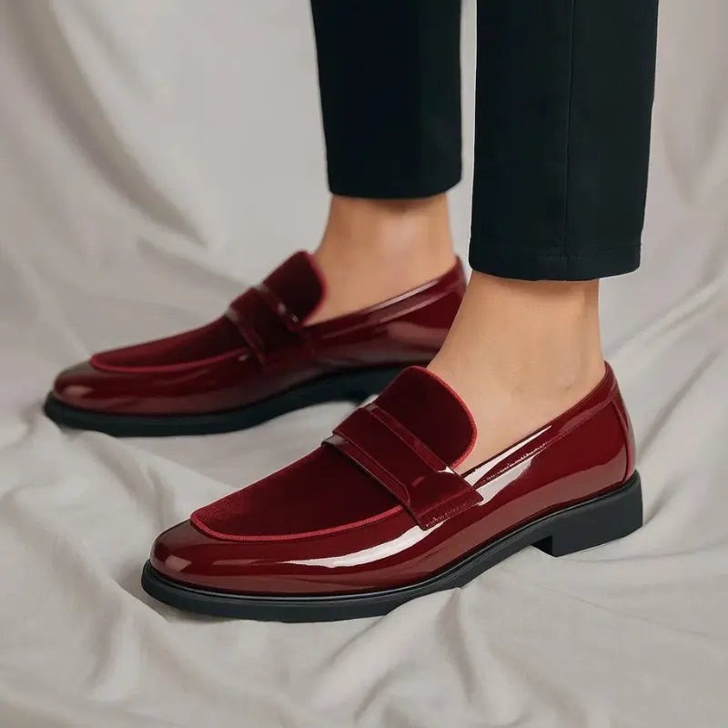 Burgundy patent loafers worn on feet, paired with dark trousers
