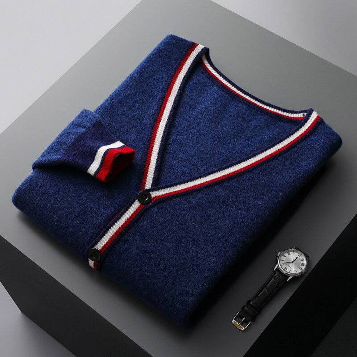 Folded navy V-neck cardigan with red and white striped trim beside wristwatch