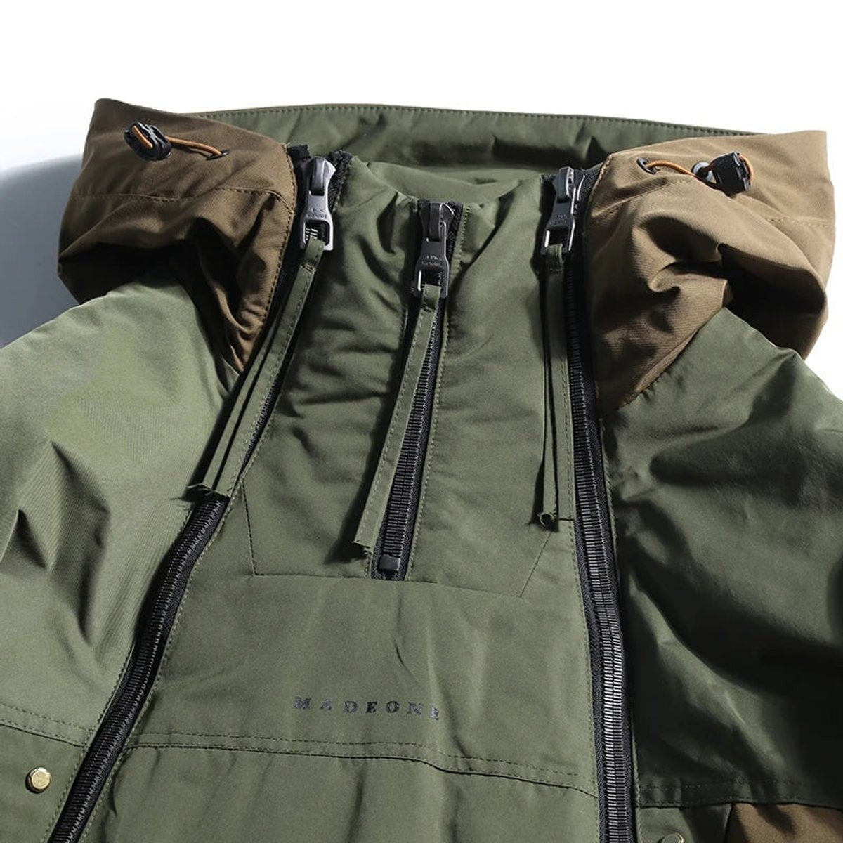 Close-up of khaki hooded jacket with triple zip fastening and MADEONE branding