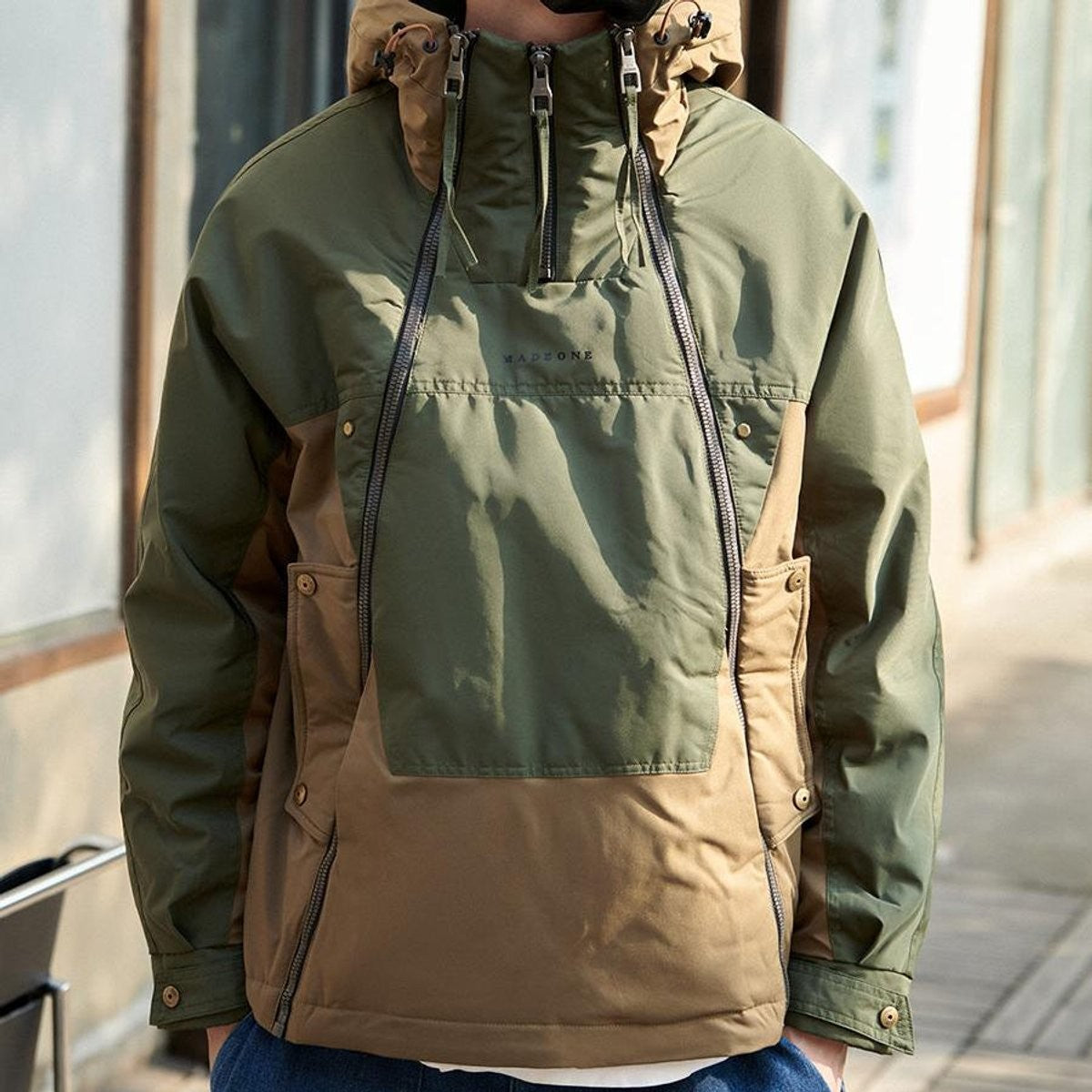 Model wearing olive and tan waterproof hooded jacket with box pockets