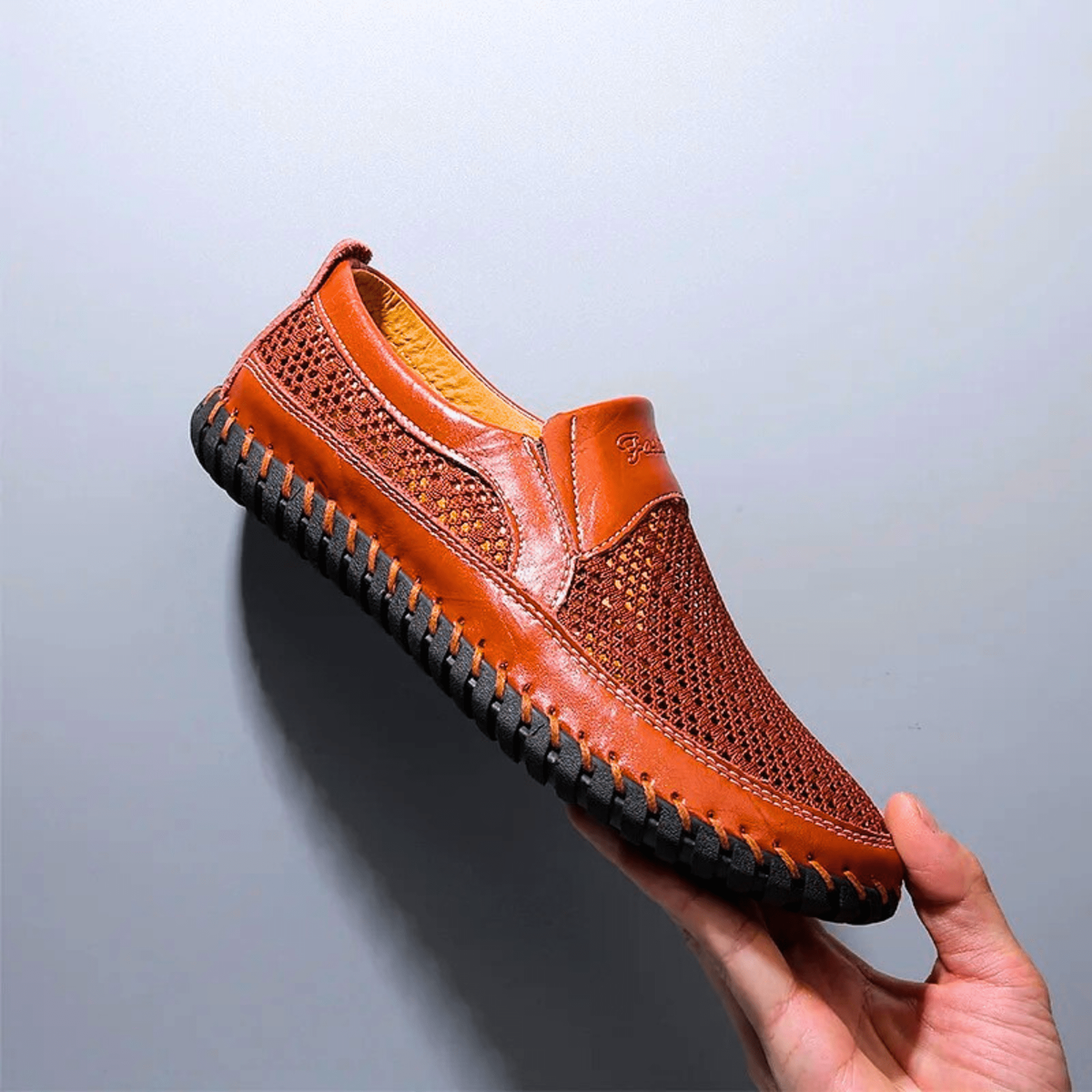 Tan leather slip-on shoe with perforated mesh detailing and whipstitched edge