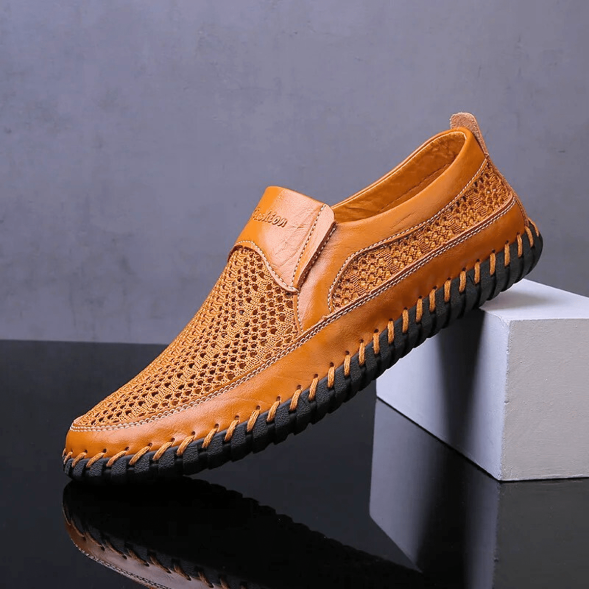 Mustard leather slip-on shoe resting on a plinth, showing woven mesh upper